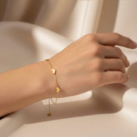 Gold bracelet with heart-shaped charms on a hand against a neutral background