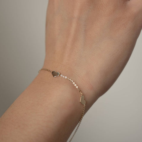 Yellow gold bracelet with heart charms on a wrist against a neutral background