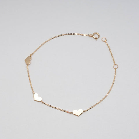 Gold bracelet with heart-shaped charms on a light gray background