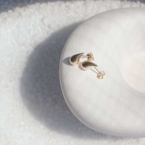 Gold tear drop  shaped earrings on a white stone surface