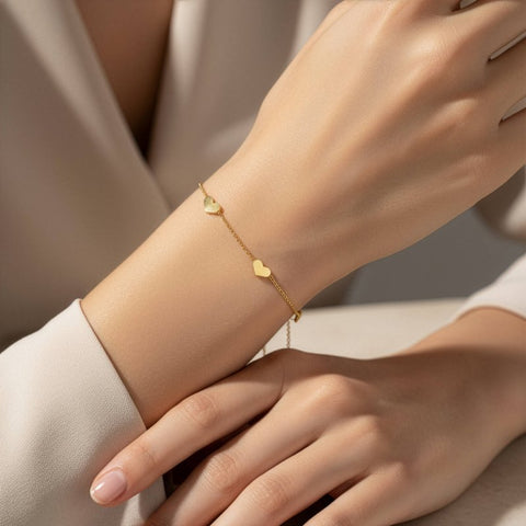 Gold bracelet with heart charms on a wrist against a neutral background
