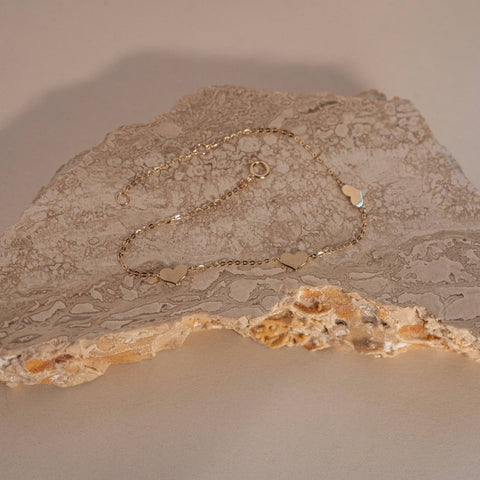 Gold necklace with heart-shaped pendants on a textured stone surface