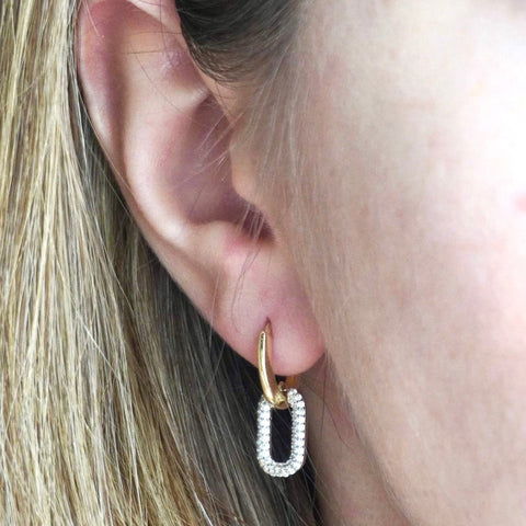 A close-up of a person wearing a gold-colored hoop earring with cubic zirconia accents.